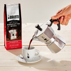 Nalévání kávy připravené v konvičce Bialetti Moka Express do bílého šálku s logem.