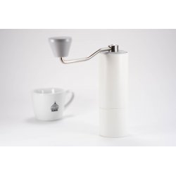 Timemore C2 ruční mlýnek na kávu v bílé barvě s šedou rukojetí. Má nerezové mlecí kameny. V pozadí šálek s logem Lázeňské kávy.