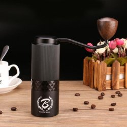 Ruční mlýnek Barista Space Premium černý položený na stole s kávou a šálkem